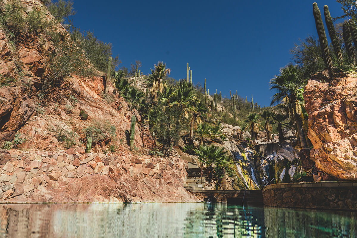 Aerial view of Castle Hot Springs, a luxurious desert retreat nestled in the Sonoran Desert in Arizona. The photo showcases the natural beauty of the surrounding mountains and the stunningly designed resort. 