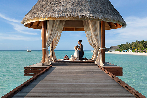 A hut located on a deck over the beach. A woman is giving another woman a head massage.